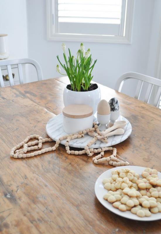 Skandinaavinen kevätkoristepöytä vaaleasta puusta valkoisista kukista ruukussa ja muita koriste -esineitä