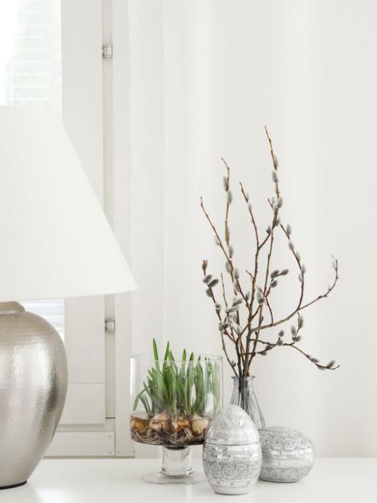Skandinaavinen kevätkoristepöytäkoriste pöytälampun vieressä Munat maljakko oksilla Lasi -astia kevätkukilla