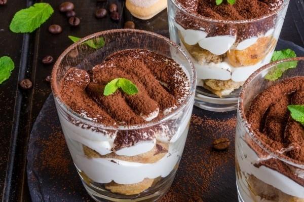 tiramisu lasissa, jossa on kaakaojauhetta, lusikkakeksejä ja mintunlehtiä