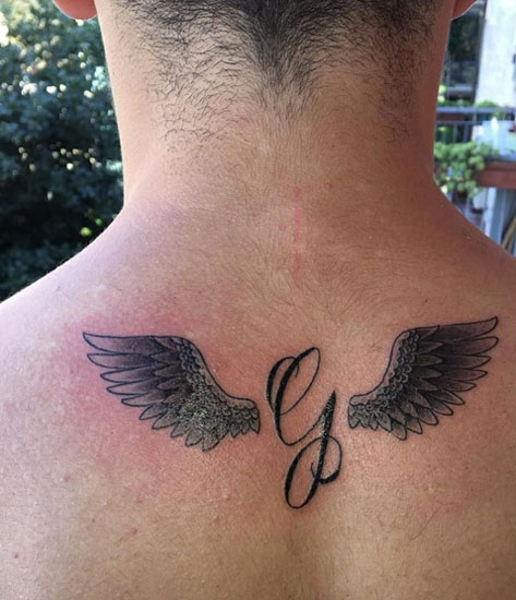 Kurzív G tetoválás szárnyakkal a hátán