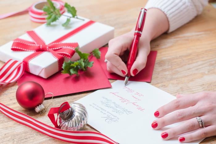 nuori nainen kirjoittaa joulukortteja punaisilla kynsillä, punaisella kynällä ja joulukoristeilla