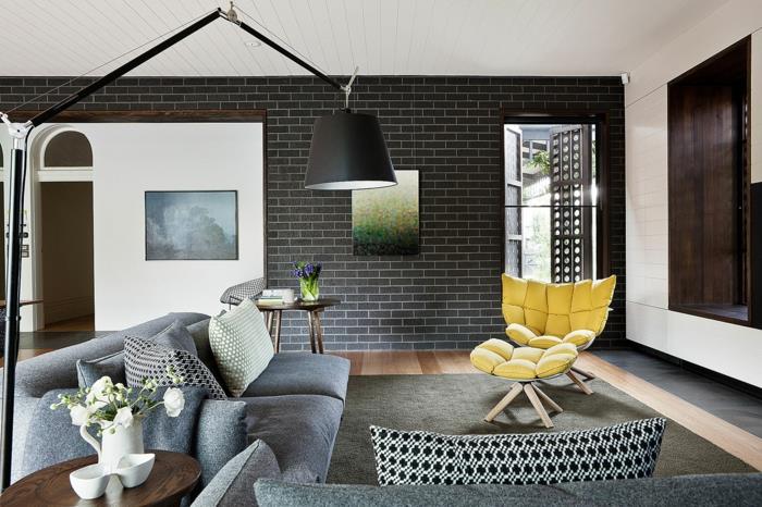 design seinät olohuone tummat seinälaatat keltainen nojatuoli harmaa sohva